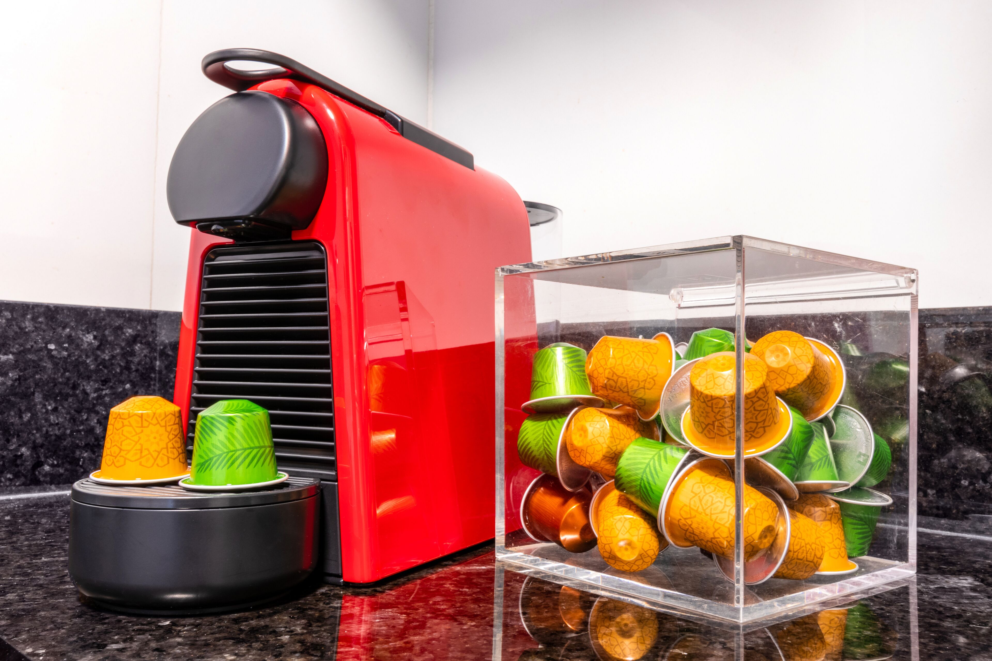 Una máquina de café roja y un recipiente de vidrio con tazas apiladas sobre una encimera de cocina.