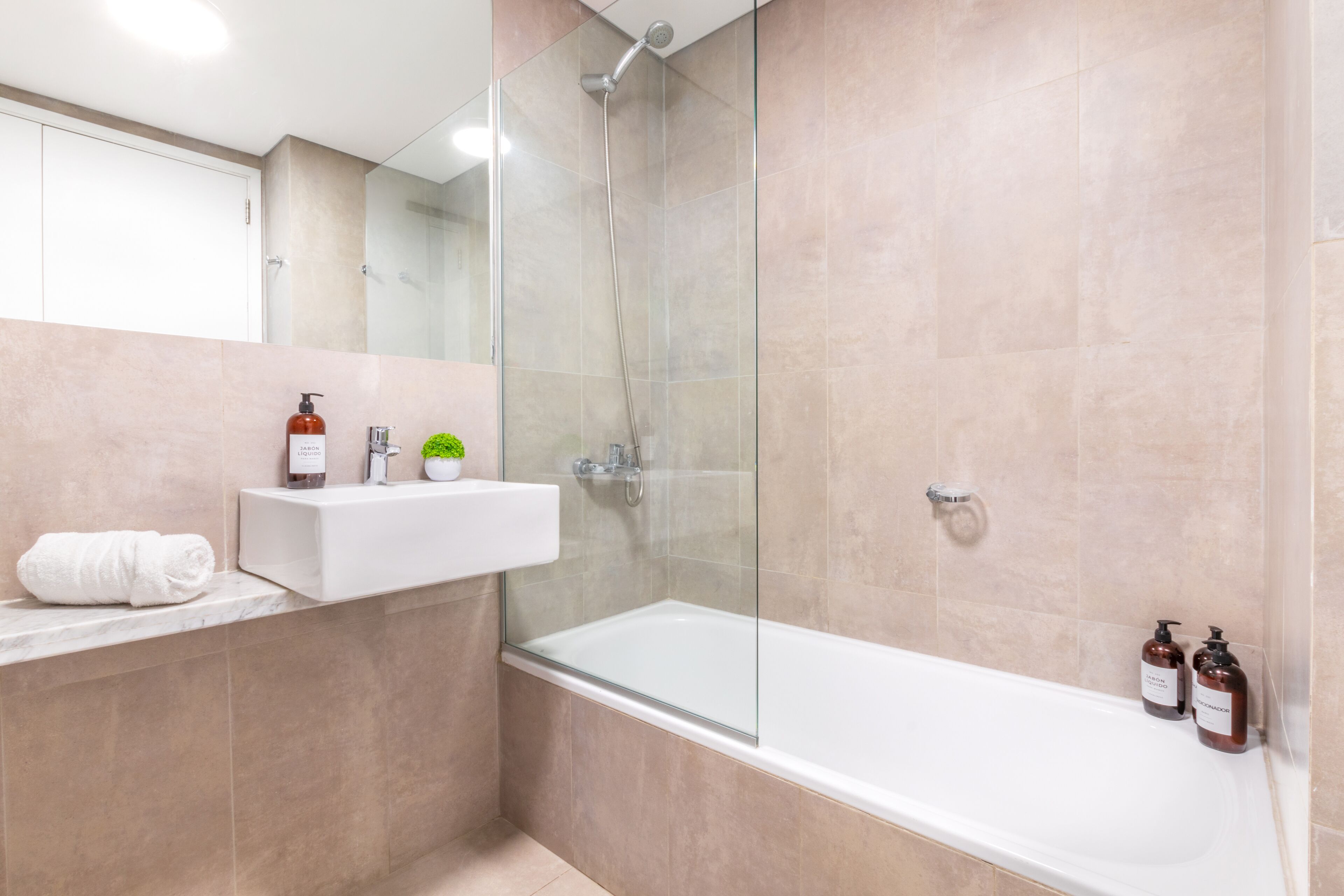 Un baño moderno con cabina de ducha de vidrio, un lavabo blanco y dos botellas de champú en una estantería.