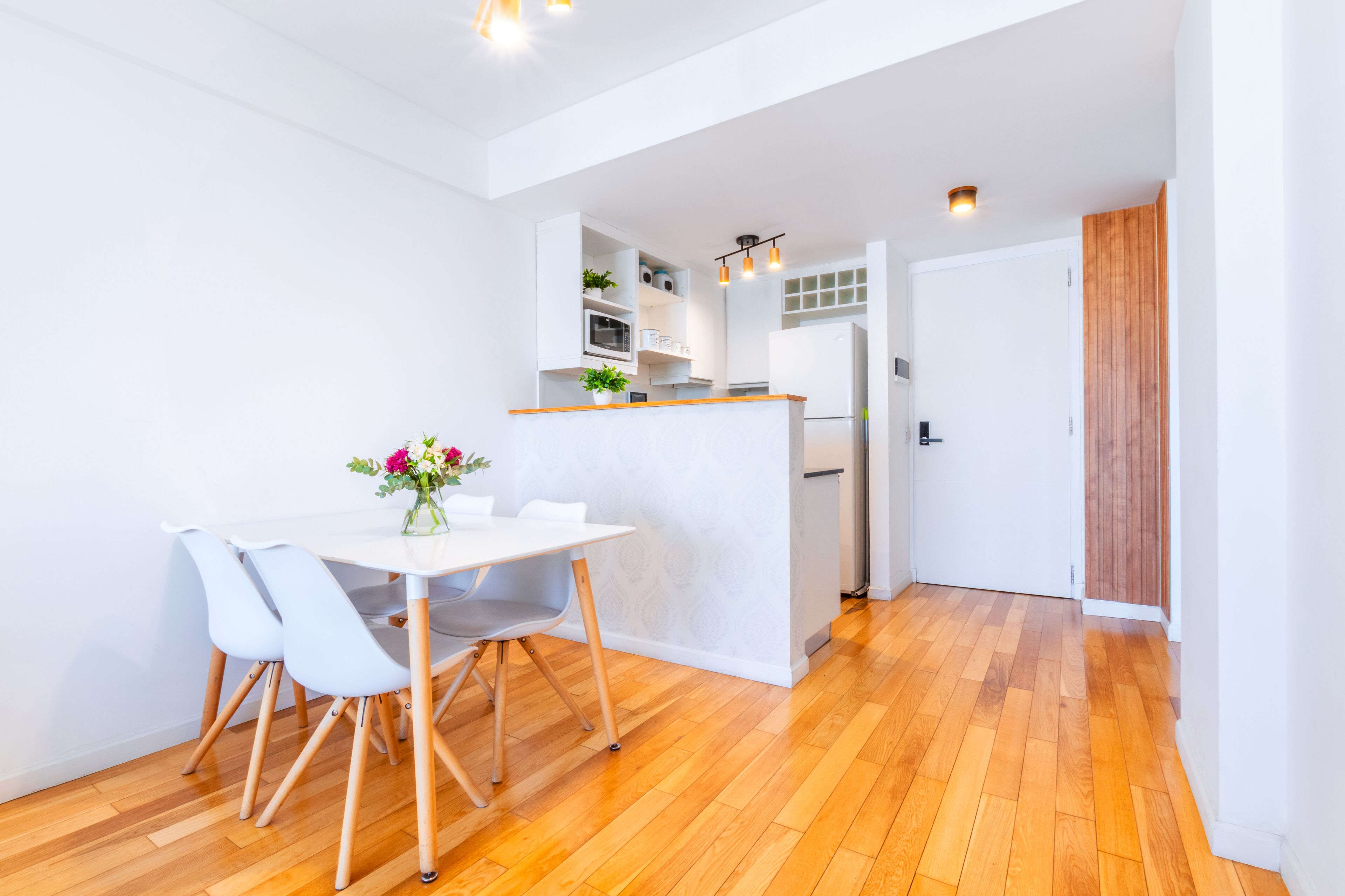 Una cocina moderna con armarios blancos, encimera de madera y comedor con mesa y sillas blancas.
