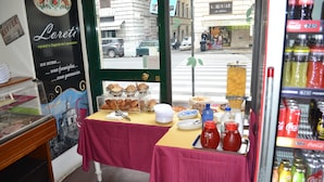 A cafe with a red tablecloth, a display of pastries, and a Coca-Cola refrigerator.