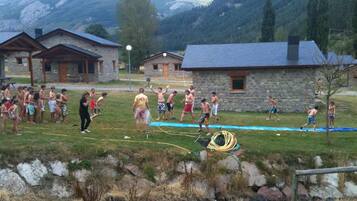 Um grupo de pessoas brincando perto de uma piscina em uma região montanhosa, com edifícios de pedra ao fundo.