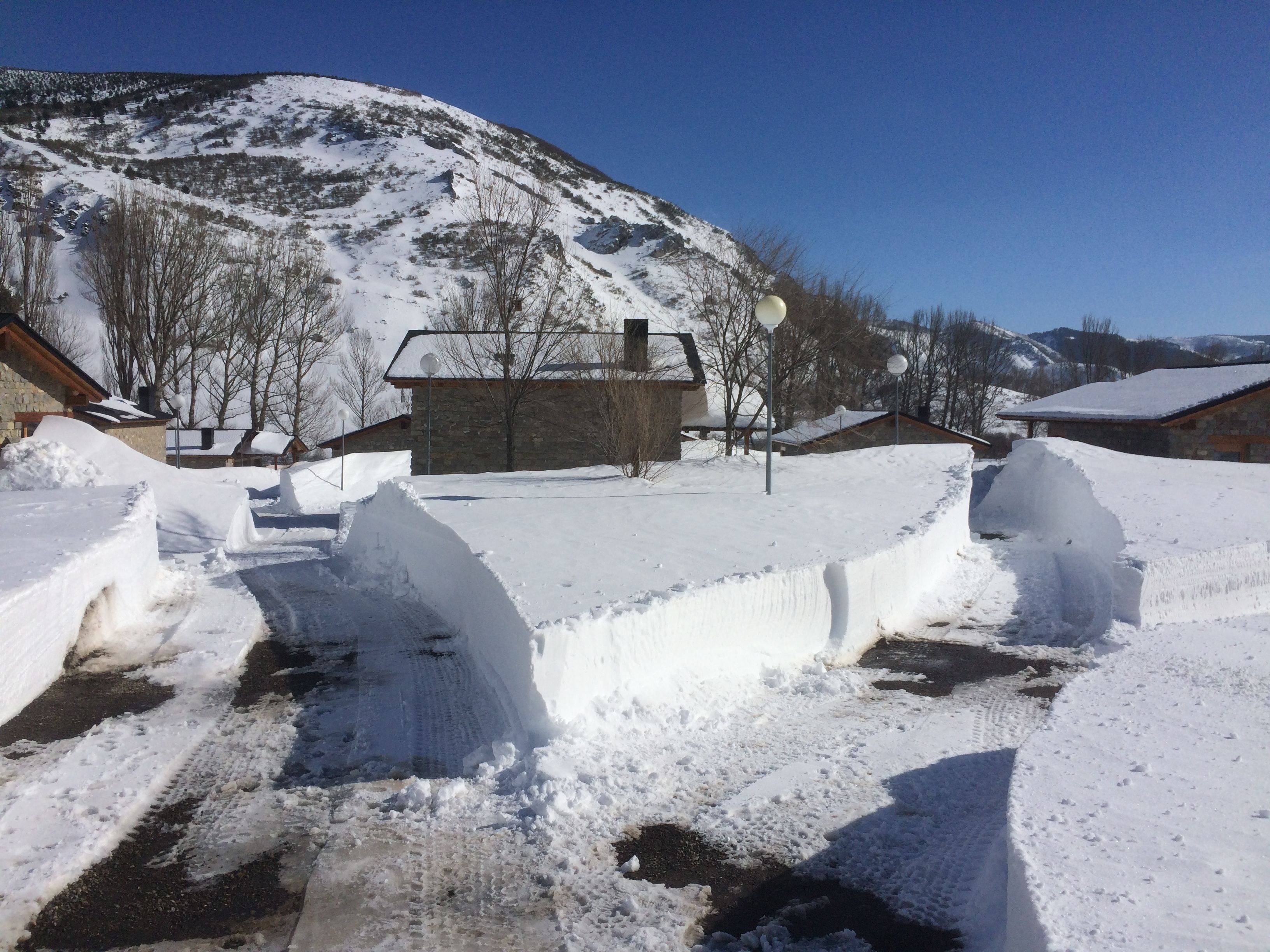 Ein schneebedecktes Dorf mit Steinhäusern, ein Berg im Hintergrund und eine teilweise freigeräumte Straße.