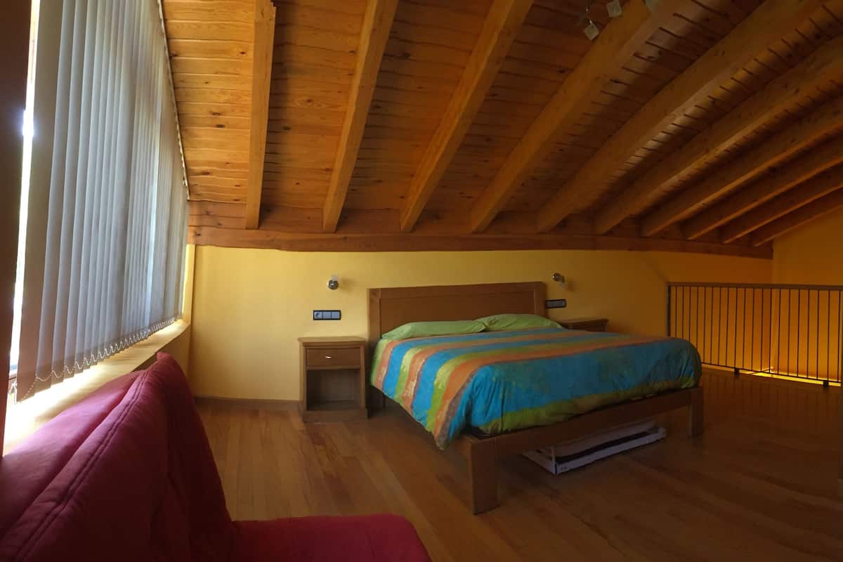Une chambre à coucher avec un plafond en bois, un lit recouvert d’une courtepointe aux couleurs vives, une armoire et une table de chevet.