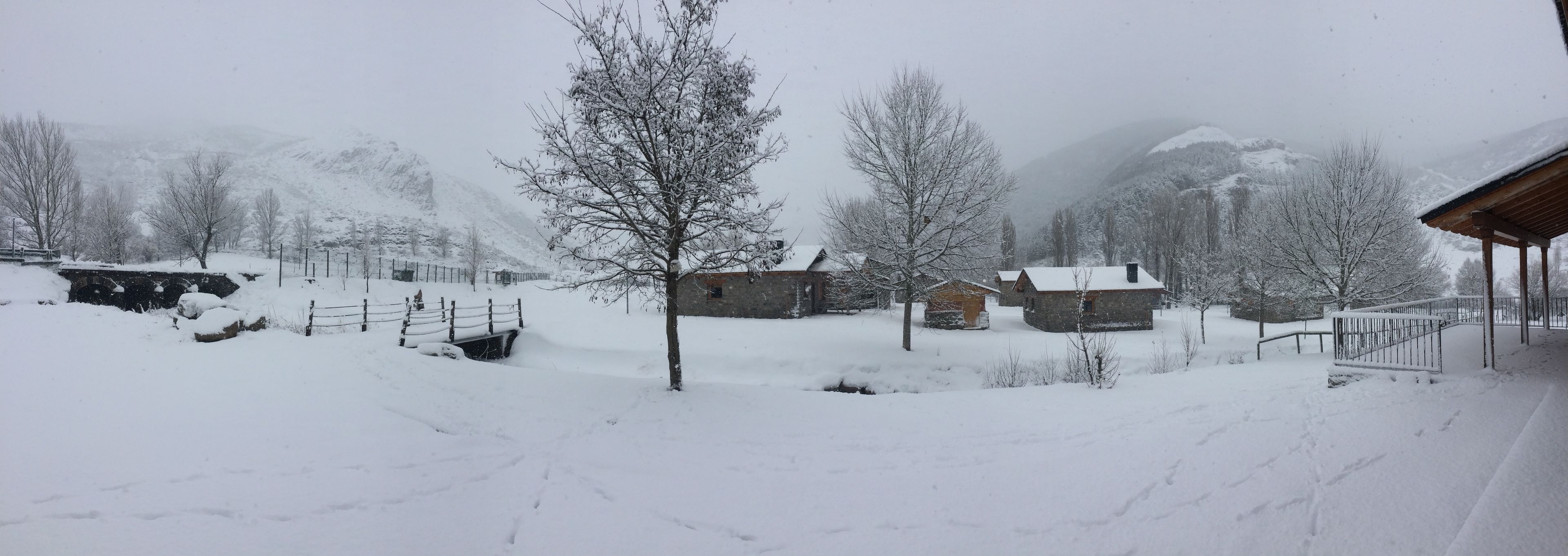 Ett snötäckt landskap med en enkel stuga, ett trästaket och ett berg i bakgrunden.