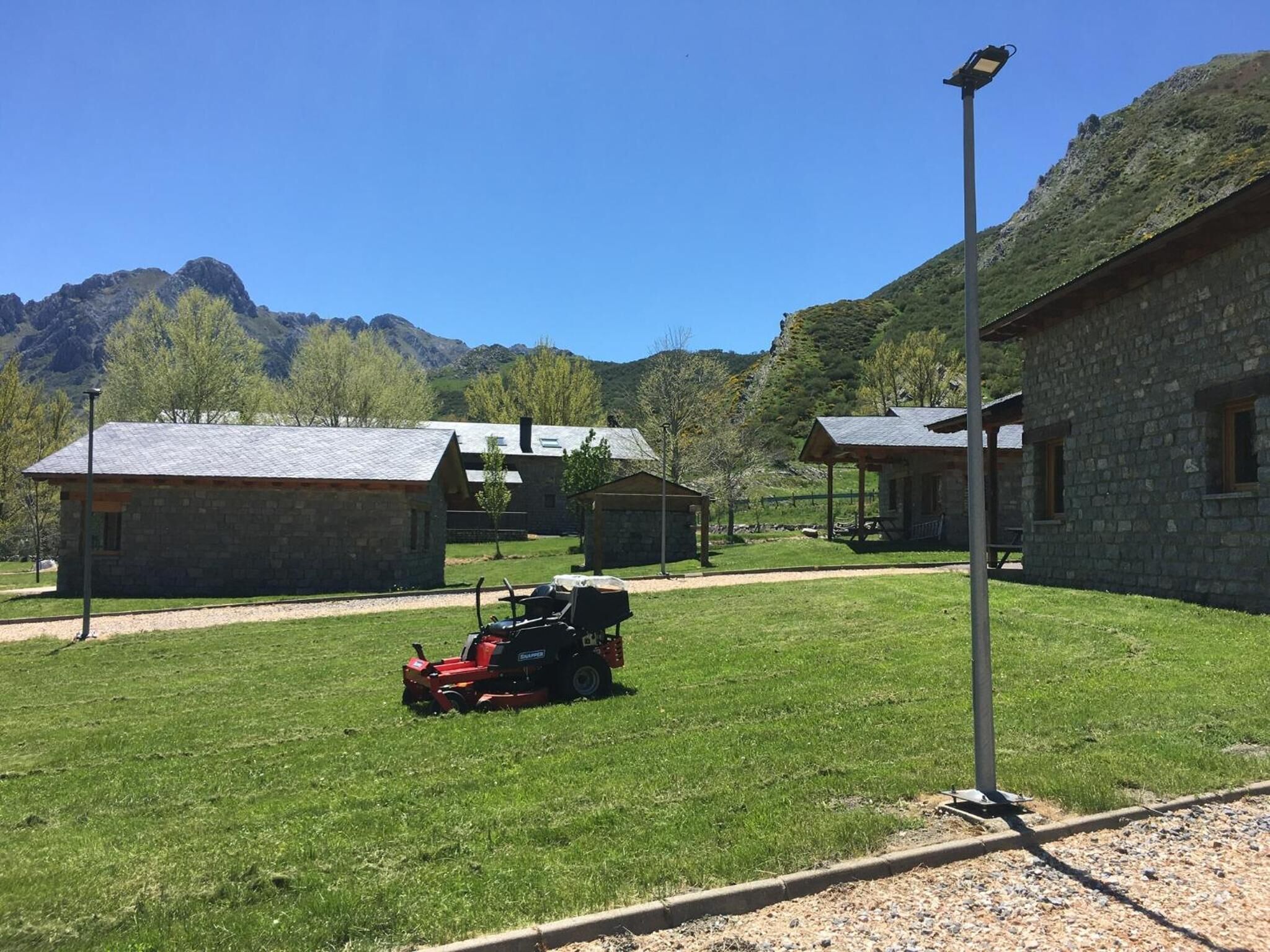 Ein Steinhaus mit Metall-Dach, eine Rasenfläche mit einem roten Rasenmäher und ein Berg im Hintergrund.