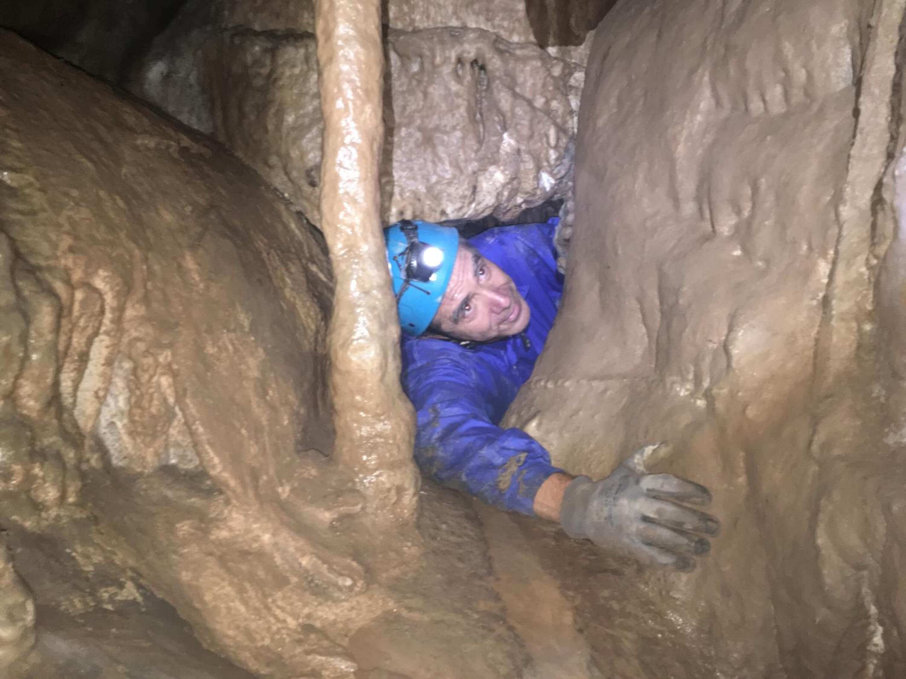 Une personne vêtue d’une veste bleue et d’un casque se trouve à l’intérieur d’une grotte aux parois irrégulières.