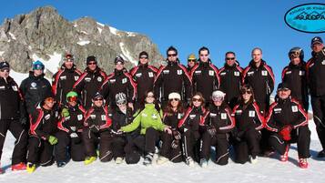 A group of people in winter sports attire posing on a snowy mountain with a rocky backdrop.