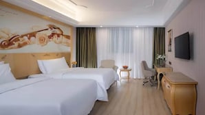 Habitación de hotel con dos camas, un escritorio, una silla, un televisor y un cuadro en la pared.