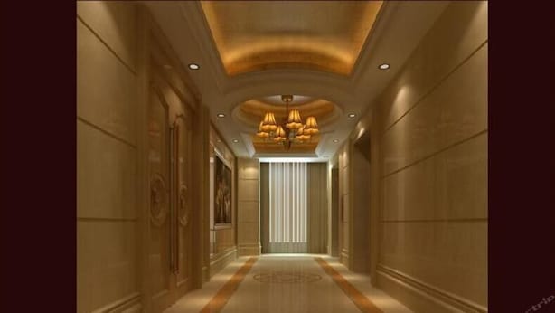 Un pasillo con piso de mármol, obras de arte en la pared y un candelabro central.