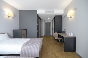 Una habitación de hotel con cama, escritorio, silla y una pequeña kitchenette.
