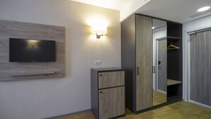 Een moderne kamer met een flatscreen-tv bevestigd aan een houten paneel, een wandlamp en een garderobe met spiegel.