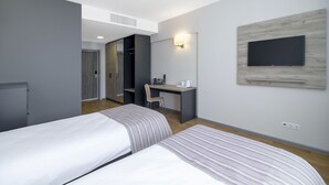Een hotelkamer met twee bedden, een bureau met stoel, een aan de muur bevestigde televisie en een inloopkast.