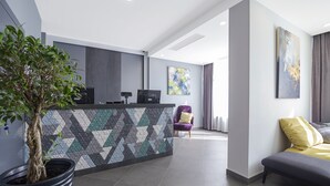 Een moderne receptie met een wand met een geometrisch patroon, een receptiebalie, een kamerplant en een zithoek met een bank en fauteuil.