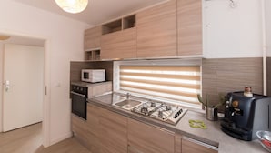 A modern kitchen with wooden cabinets, a gas stove, a microwave, and a coffee machine. - Thomas Apartments (Brasov)