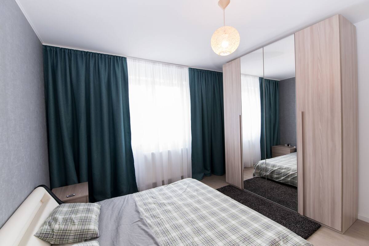 A modern bedroom with a bed, a nightstand, a mirror, and a wardrobe.