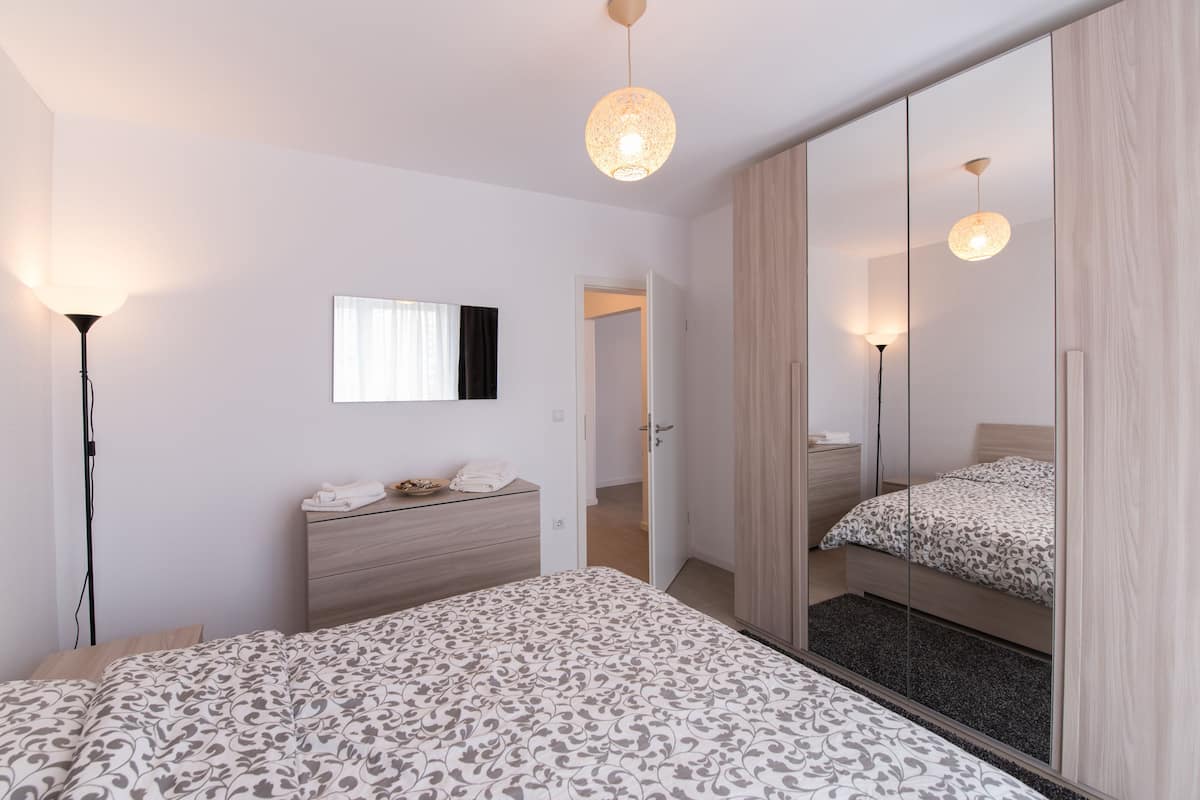 A modern bedroom with a large bed, bedside tables, a dresser, and a mirror.