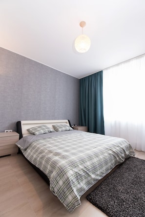A modern bedroom with a bed, nightstands, a rug, and a hanging light fixture. - Thomas Apartments (Brasov)