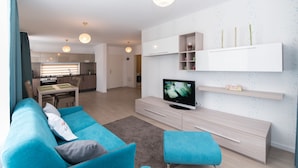 A modern living room with a blue sofa, a TV, and a kitchen in the background. - Thomas Apartments (Brasov)