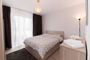 A modern bedroom with a large bed, a bedside table with towels, and a floor lamp. - Thomas Apartments (Brasov)
