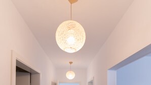 A hallway with a wooden floor, white walls, and a hanging pendant light fixture. - Thomas Apartments (Brasov)