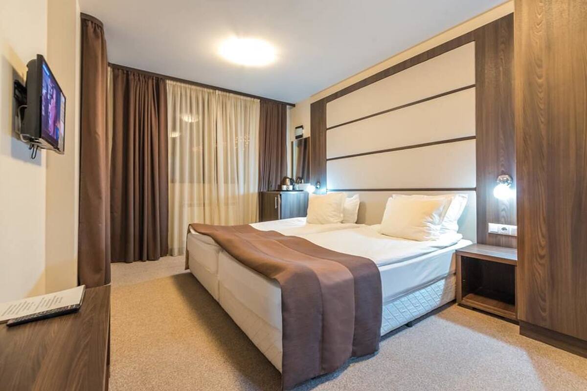 Una habitación de hotel moderna con una cama grande, un televisor de pantalla plana en la pared y una mesita de noche con una lámpara.