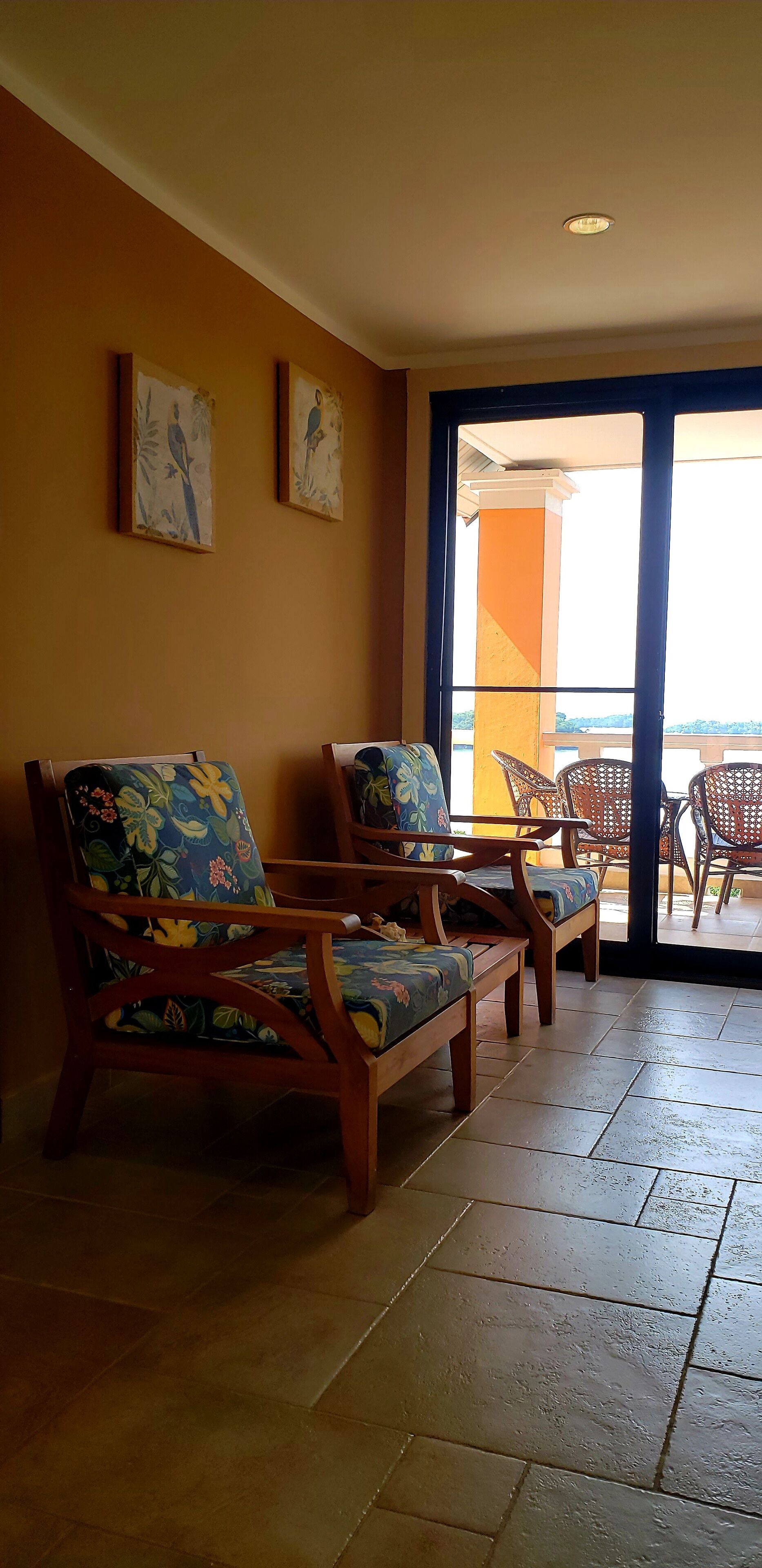 Une pièce avec des chaises en bois et une table, un balcon avec une balustrade, et deux tableaux accrochés au mur.