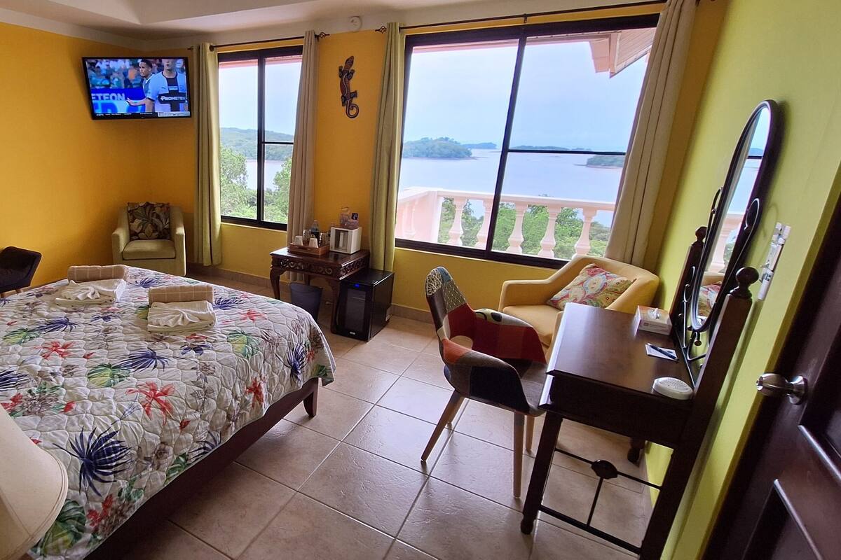 Een hotelkamer met een bed, een bureau, een stoel, een televisie en een groot raam met uitzicht op zee.