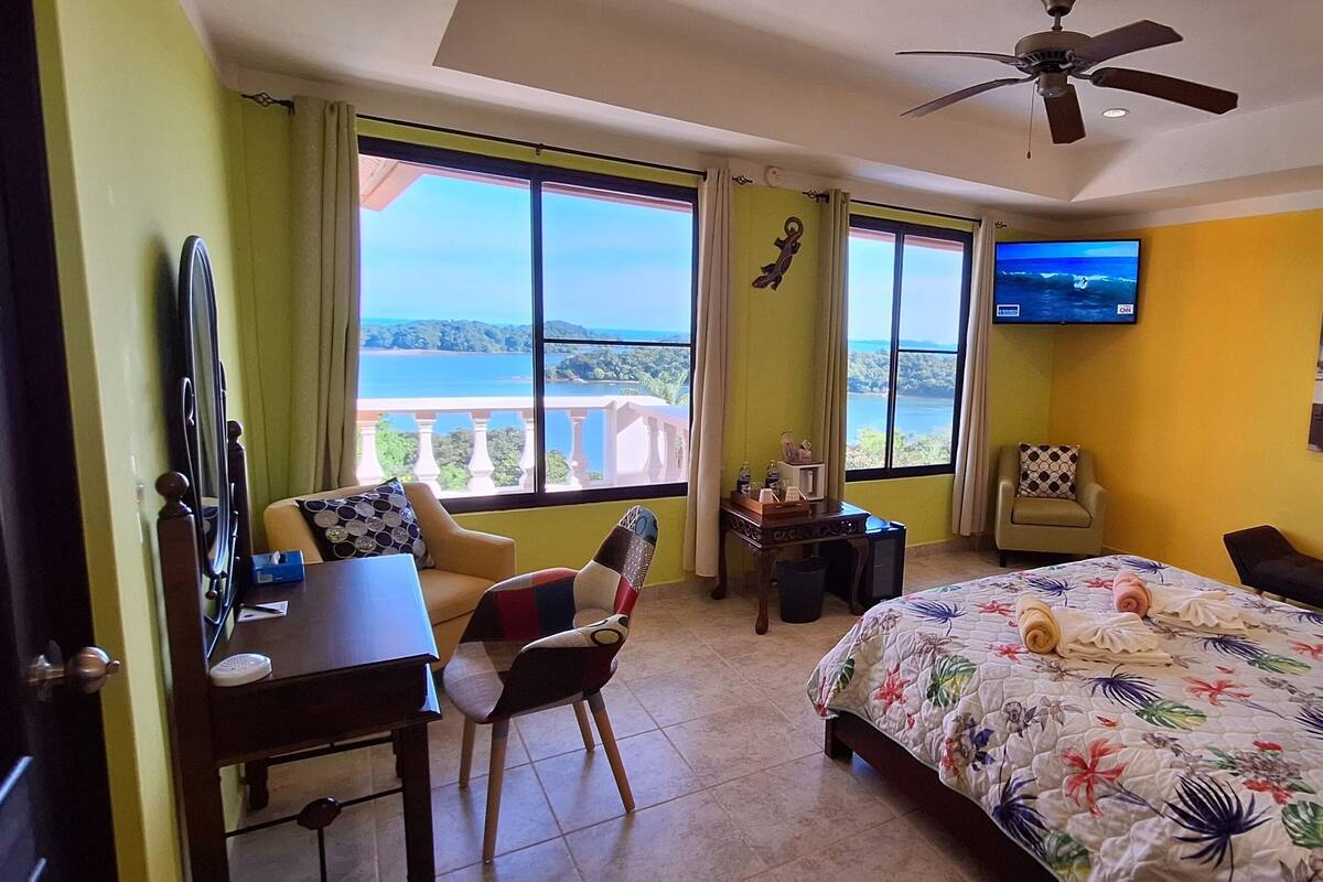 Een hotelkamer met een bed, een bureau, een stoel, een televisie en een balkon met uitzicht op zee.