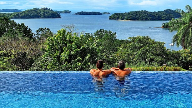 Une piscine offrant une vue sur une vaste étendue d’eau et des îles, le tout entouré d’une végétation luxuriante.
