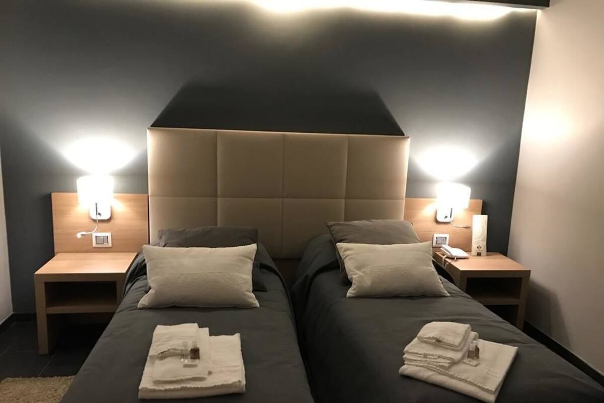 Ein Hotelzimmer mit zwei Betten, jeweils mit Kopfteil, Nachttischen und Lampen.