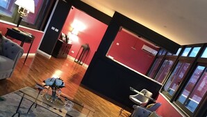 Un salon moderne avec un canapé gris, un tapis à motifs et une table basse. Un mur d’accent rouge et une fenêtre avec vue complètent l’ensemble.