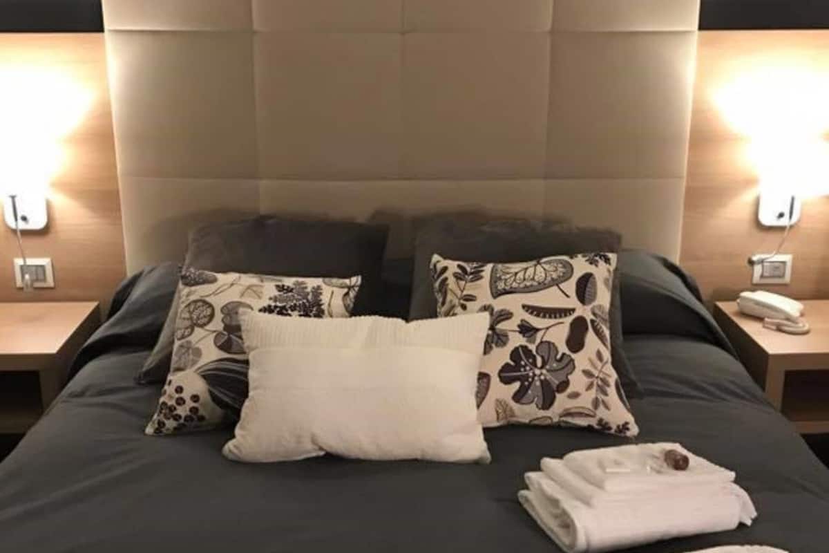 Ein ordentlich bezogenes Bett mit Kissen in Blumenmuster, einem weißen Kissen und gefalteten Handtüchern auf einer dunkel gefärbten Bettdecke.