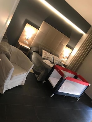 A modern hotel room with a bed, a sofa, and a small table with a lamp.