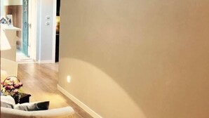 Un couloir aux murs de couleur neutre, doté d’un plancher en bois et agrémenté d’un canapé blanc sur lequel est posé un vase de fleurs.