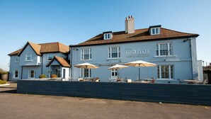 A two-story building with a sign reading "The Manor Hotel & Restaurant." There are outdoor tables and umbrellas, and a brick wall in front. - Berwick Manor Hotel (Rainham)