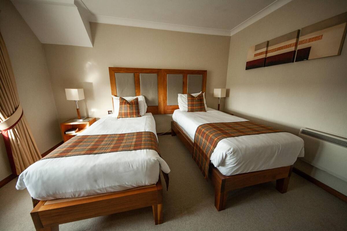A hotel room with two single beds, a wooden headboard, a large mirror, and a painting on the wall.