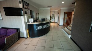 A reception area with a curved reception desk, a flat-screen TV, a couch, and a staircase leading to an upper floor. - Berwick Manor Hotel (Rainham)