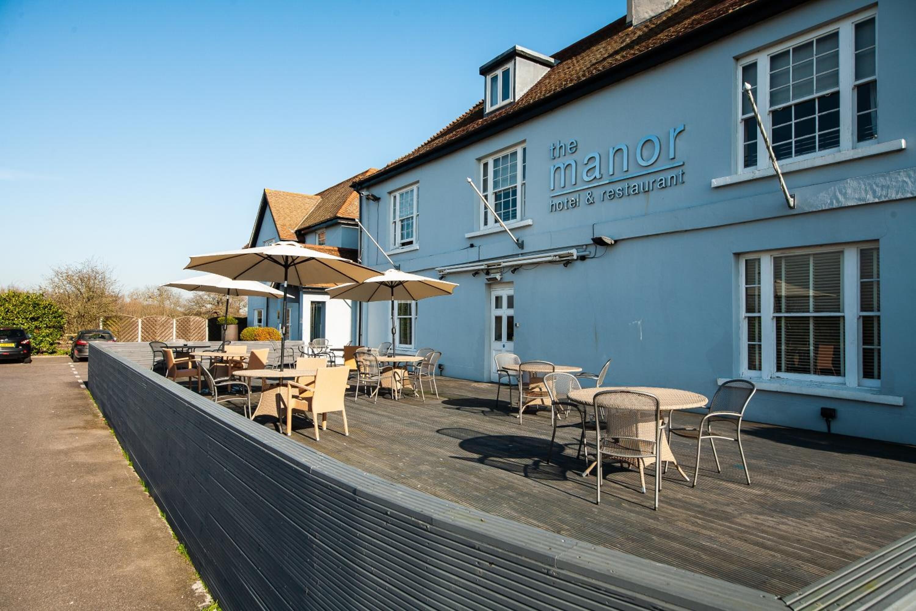 A blue building with the sign "the manor hotel & restaurant" and outdoor seating with umbrellas.