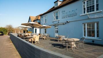 A blue building with the sign "the manor hotel & restaurant" and outdoor seating with umbrellas.