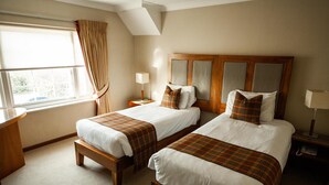 A hotel room with two single beds, a wooden headboard, a window with curtains, a bedside table with a lamp, and a carpeted floor. - Berwick Manor Hotel (Rainham)