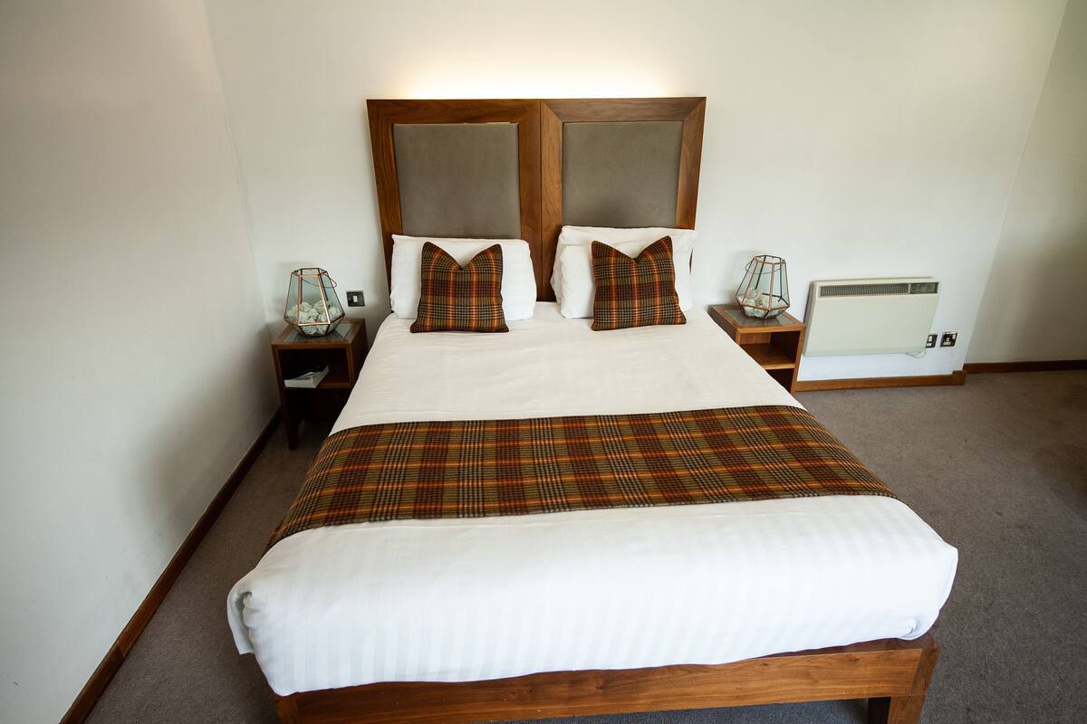 A neatly made bed with a plaid bedspread, two matching pillows, and a wooden headboard.