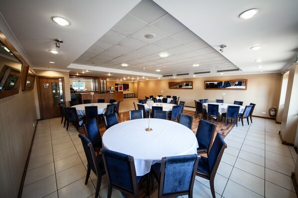 A conference room with round tables and blue chairs, equipped with ceiling lights and a wooden floor.