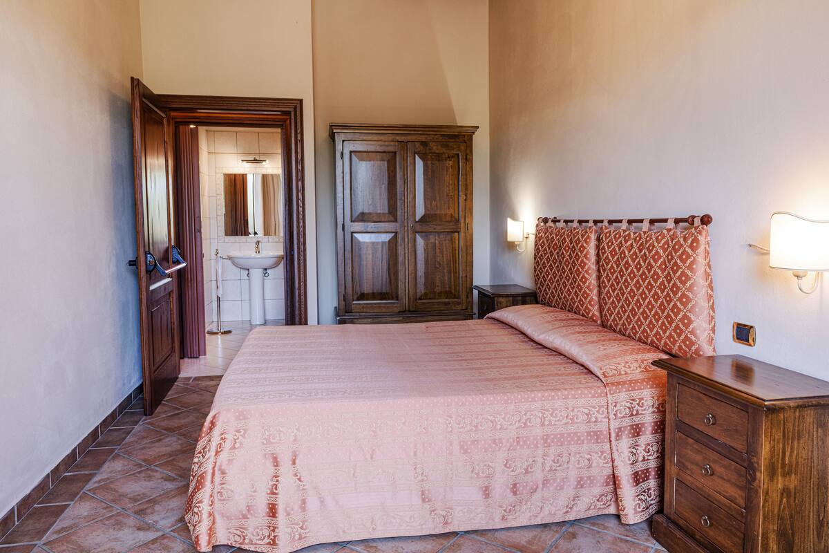 A bedroom with a bed, a wardrobe, a nightstand, and a bedside lamp.