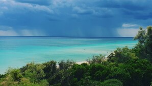 Un paysage côtier avec une plage, une végétation luxuriante et une mer bleue et limpide sous un ciel nuageux.