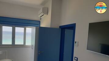 A room with a large window overlooking the sea, a blue door, a white chair, and a wall-mounted air conditioner.