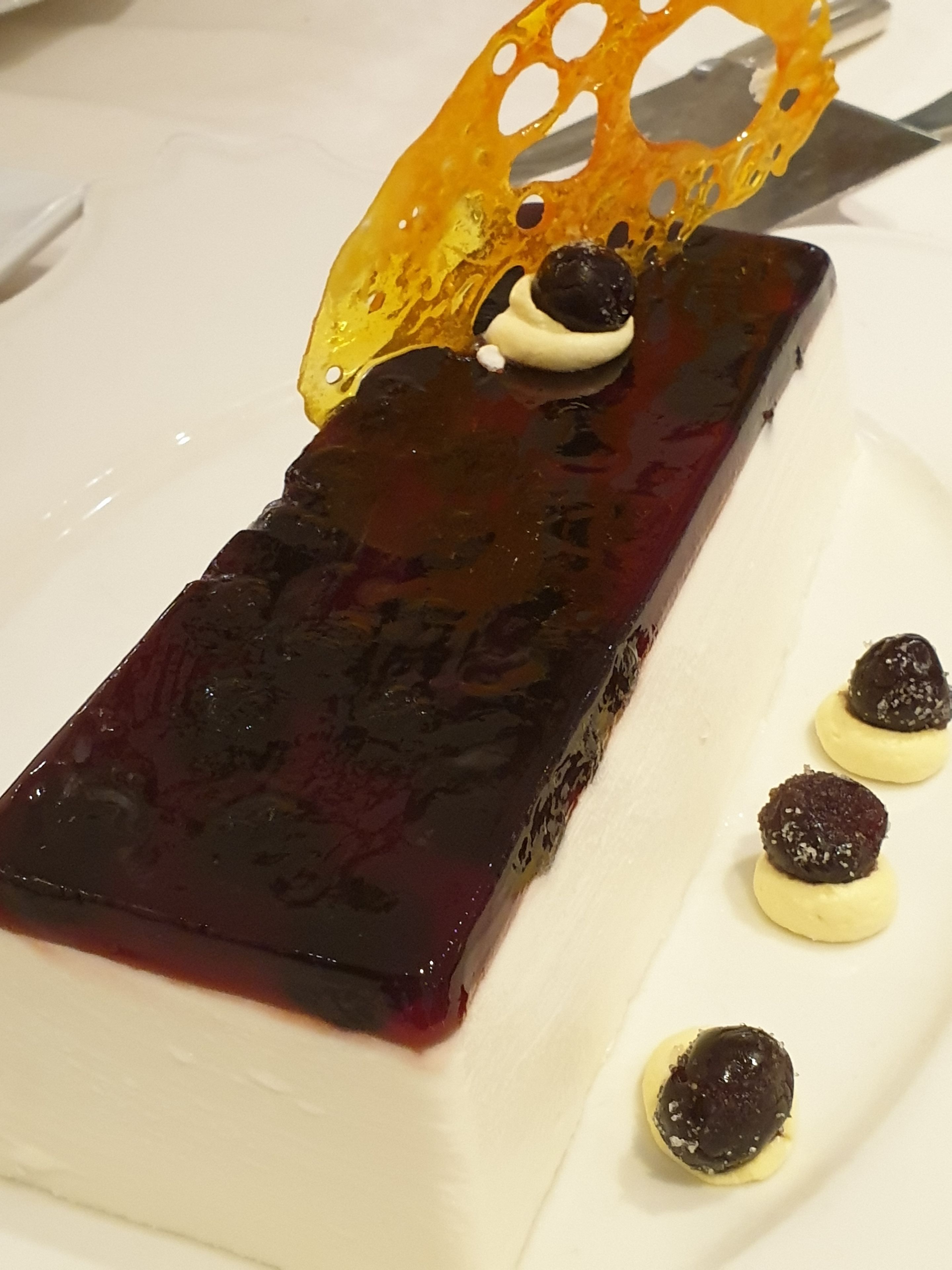 Un dessert avec une garniture rouge brillante, un élément décoratif jaune et de petites confiseries rondes, le tout présenté sur une assiette blanche.