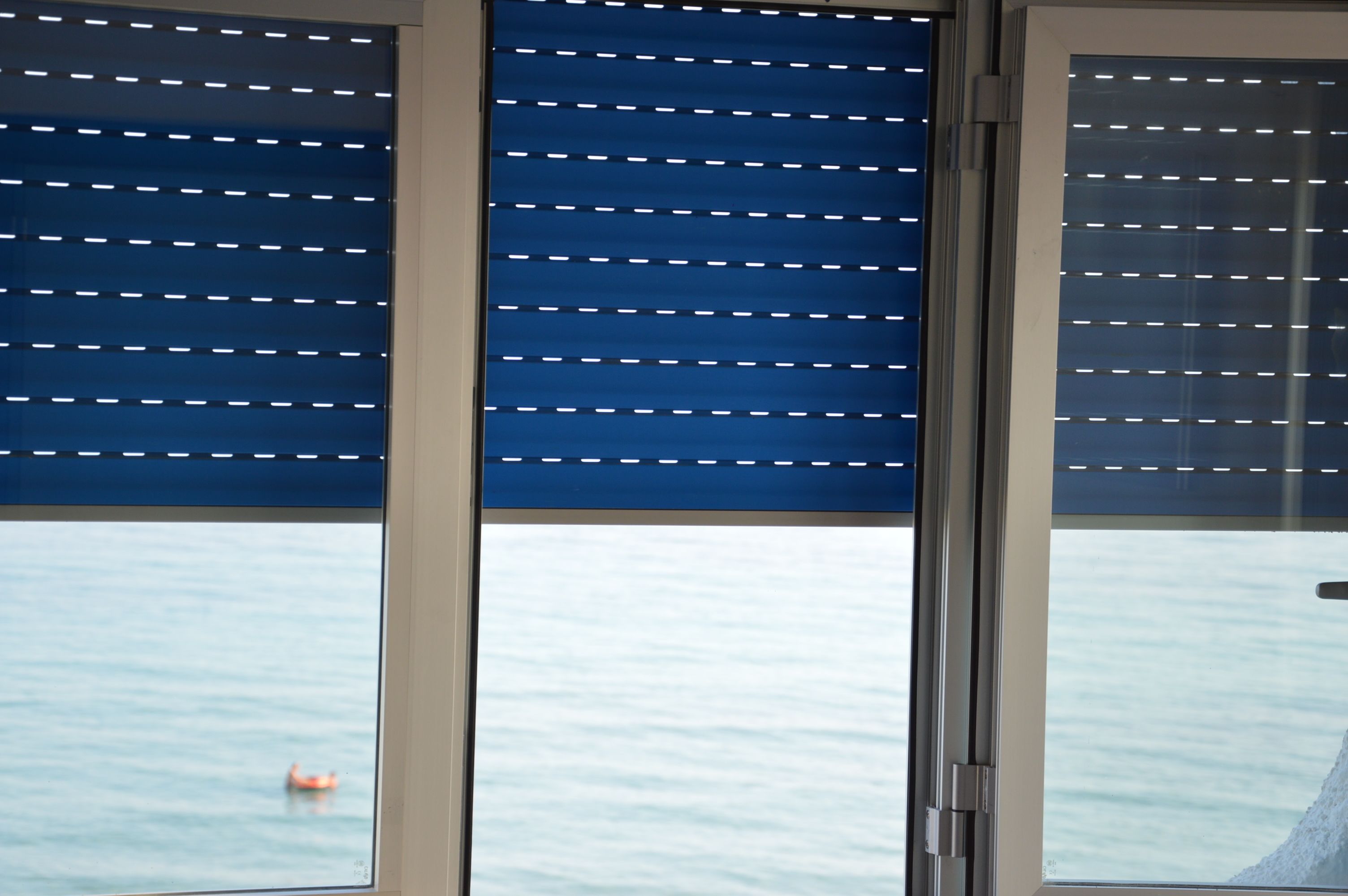 A window with horizontal blinds, a view of calm water, and a small orange buoy.