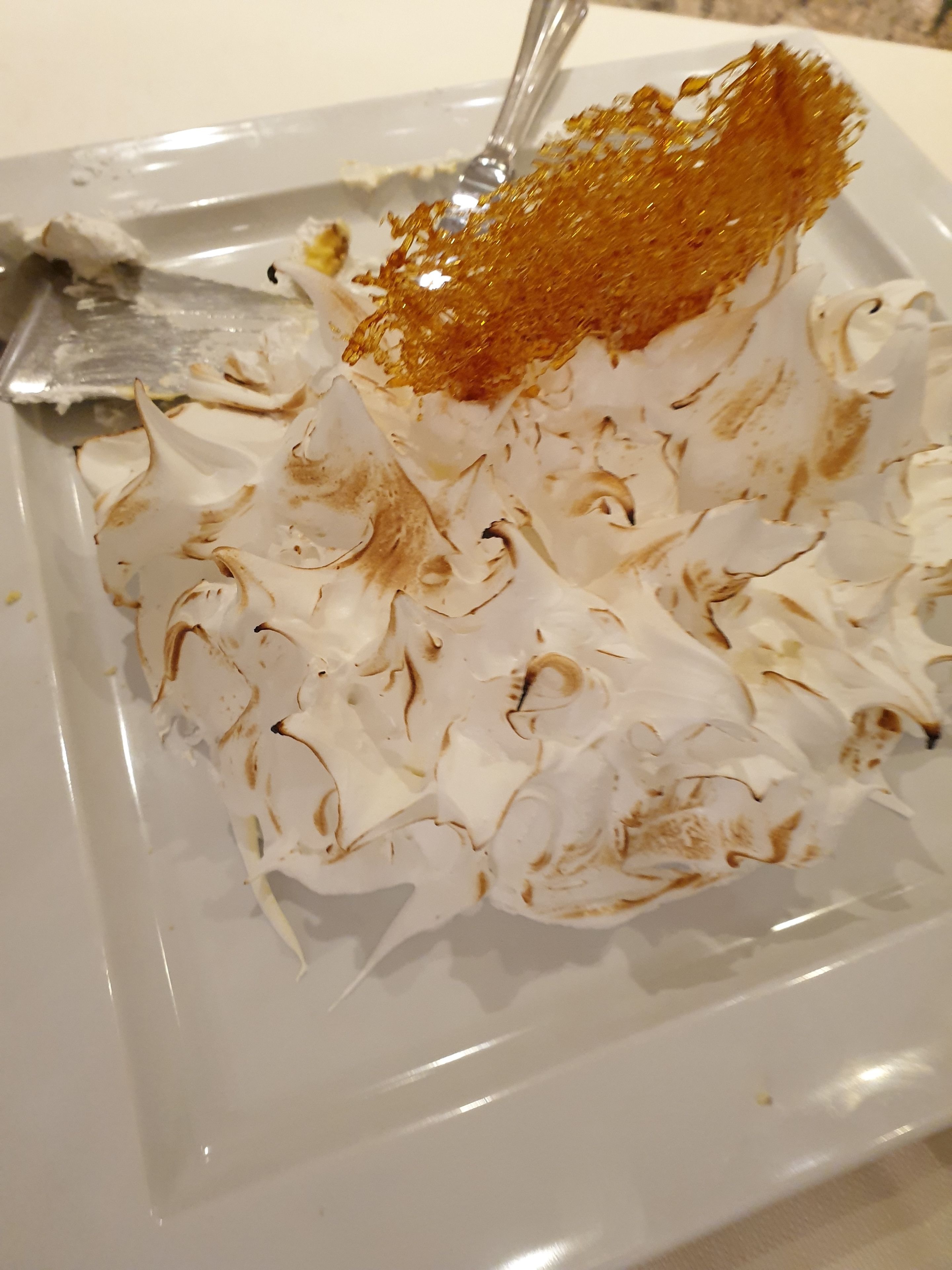 Un postre con una capa dorada, posiblemente merengue caramelizado, sobre un plato blanco.