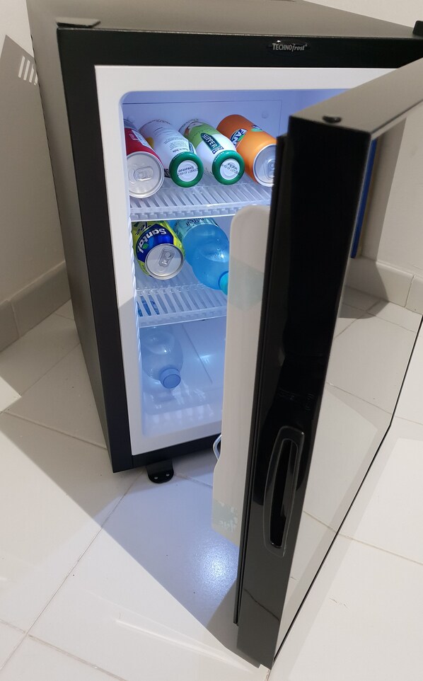 A mini-fridge with a freezer compartment containing various beverages and a water bottle.