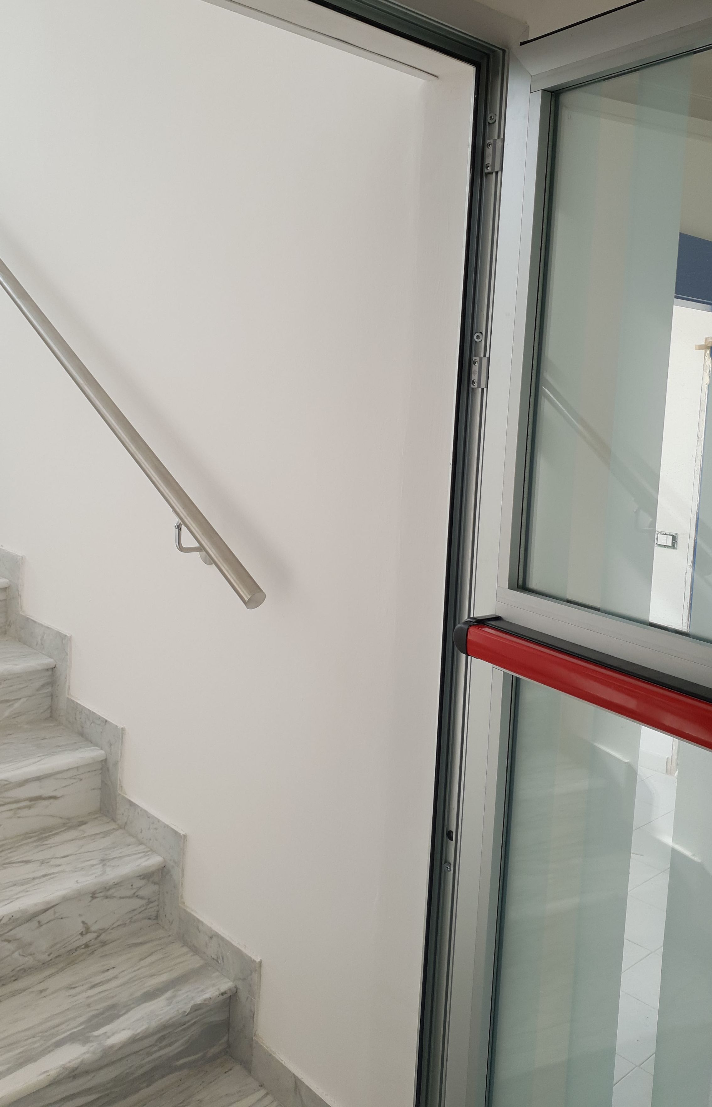 A staircase with marble steps and a glass door with a red handle.